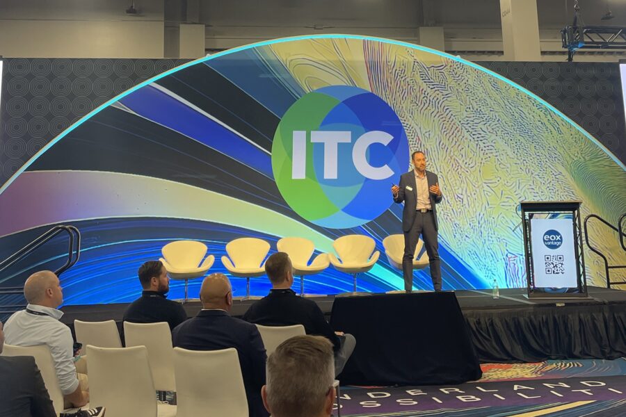 Travis Roe standing on a stage in front of a small audience in front of a colorful backdrop at ITC 2025.